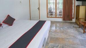 Une chambre d’hôtel avec un lit, une télévision, une chaise en bois et une vue sur l’extérieur par une fenêtre munie de rideaux.