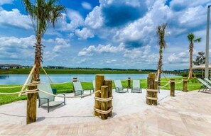 Zona junto a la piscina con sillones de descanso y postes de madera, cielo despejado y una masa de agua al fondo.
