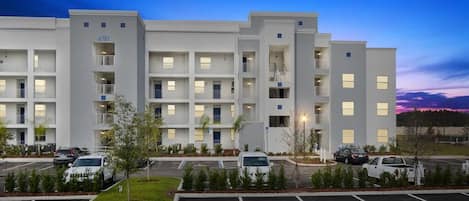 Un hôtel à plusieurs étages doté d’un parking et d’un espace paysager agrémenté de petits arbres.