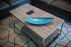 Una sala moderna con una mesa de centro de madera, un cuenco de vidrio azul y dos controles remotos.
