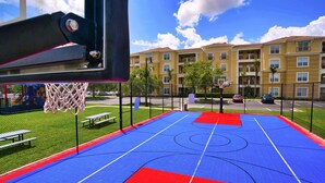 Ein Basketballplatz im Freien mit Netz, Bänken und einer Umzäunung.