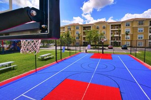 Ein Basketballplatz im Freien mit Netz, Bänken und einer Umzäunung.