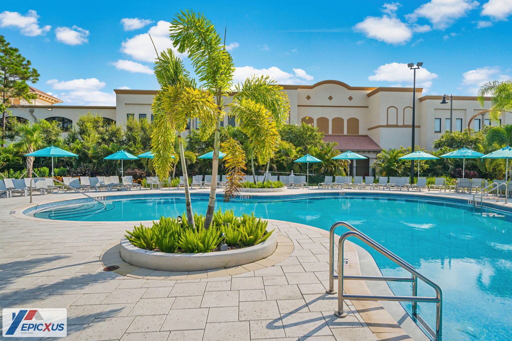 A swimming pool with lounge chairs and umbrellas, surrounded by palm trees and a building with arched windows.