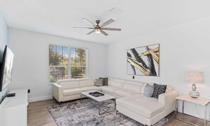 A modern living room with a white sofa, a coffee table, a TV, and a ceiling fan. - The Epic 12108 Lake View Vista Cay Resort Orlando Florida (Orlando)