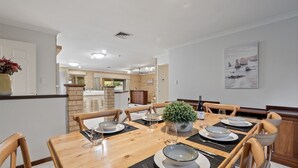 A dining area with a wooden table set for six, surrounded by chairs. A potted plant is on the table, and a wine bottle is visible. The room has a brick wall and a painting on the wall. - Gem on Jones - Abbey Beach (Abbey)