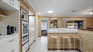 A modern kitchen with a brick accent wall, white cabinetry, and a central island with stools. - Gem on Jones - Abbey Beach (Abbey)