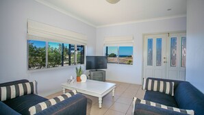 A living room with two sofas, a coffee table, a TV, and large windows with a view of the sea.