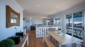 A modern kitchen with a dining area, large windows, and a view of the sea.