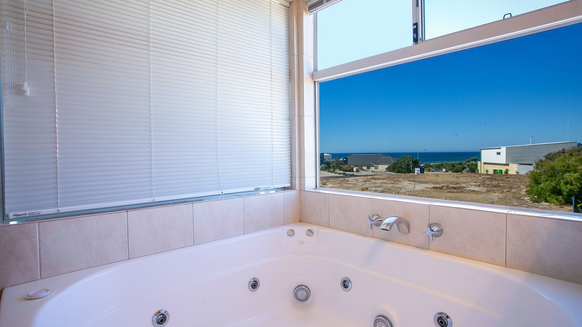 Un baño con una bañera grande, una ventana con persianas y vista al mar.