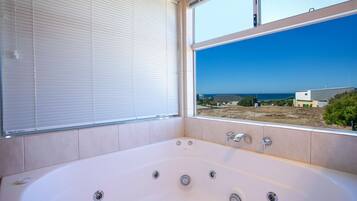 Un baño con una bañera grande, una ventana con persianas y vista al mar.