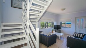 A modern interior with a staircase, a flat-screen TV, and a view of the sea.