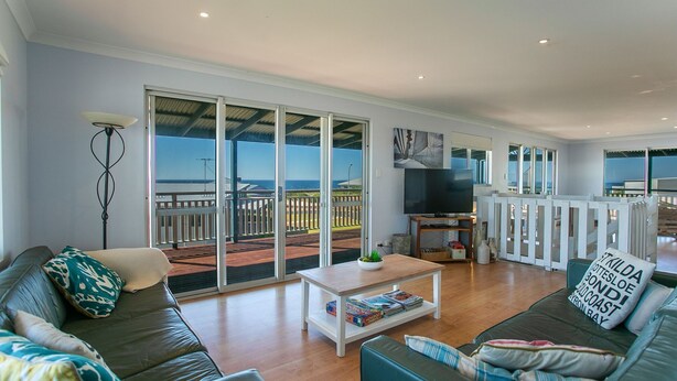 A spacious living room with a large sliding glass door leading to a balcony with a view of the ocean. There is a sofa, a coffee table, and a television.