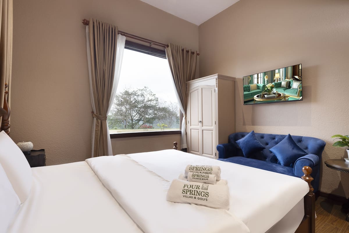 A hotel room with a bed, a blue sofa, a TV, and a window with curtains.