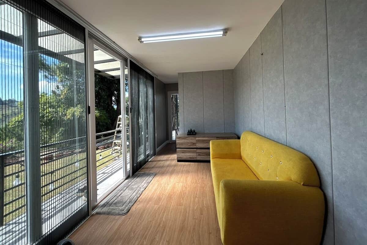 A modern living room with a yellow sofa, large sliding glass doors, and a view of the outdoors.
