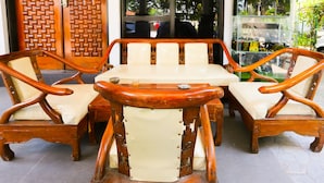 A wooden dining set with cushioned chairs and a table, positioned in front of a wooden door and glass display case. - OYO 93145 Pondok Alam Syariah (Depok)