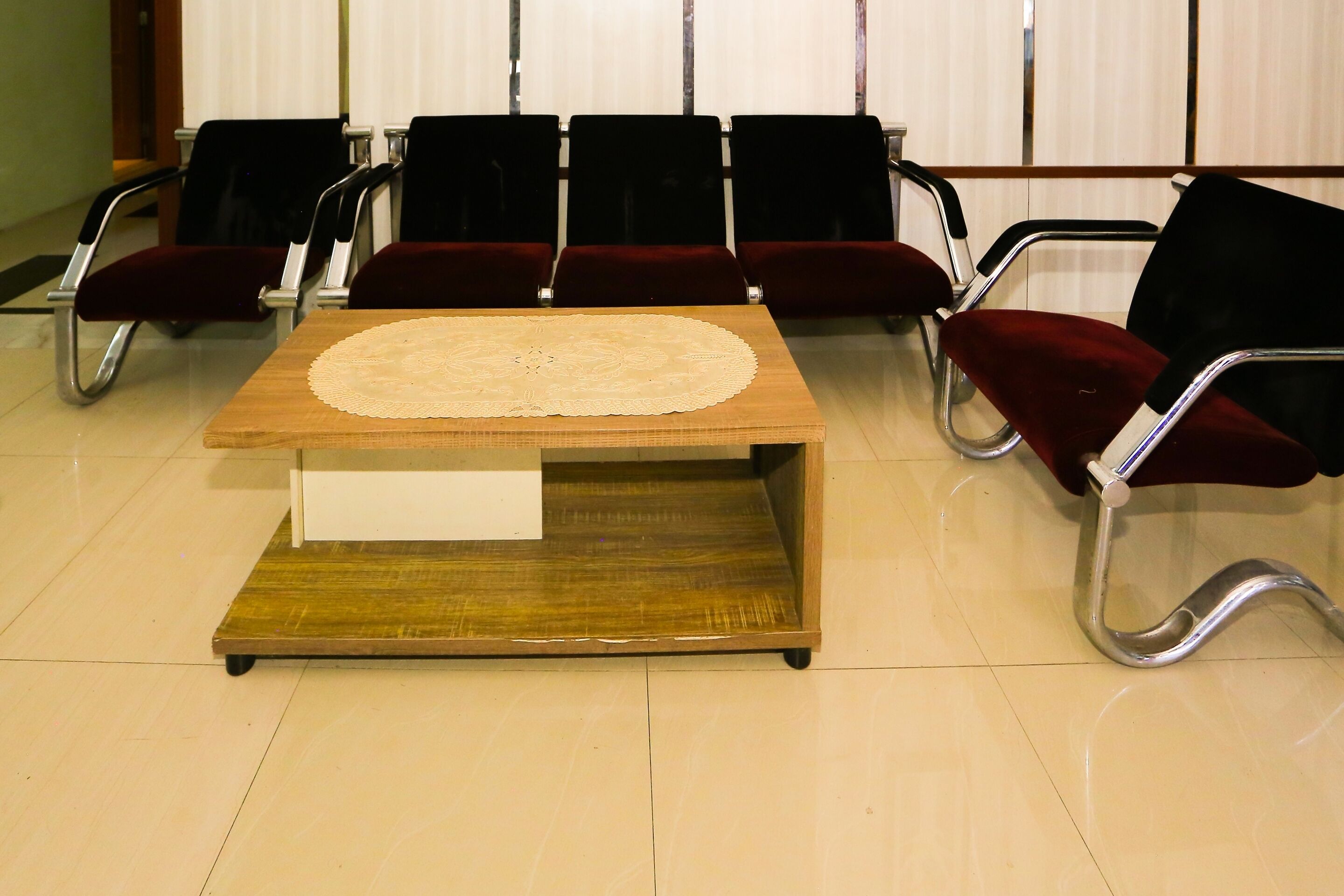 Une salle d’attente avec une table en bois, des fauteuils en velours rouge et un sol carrelé.