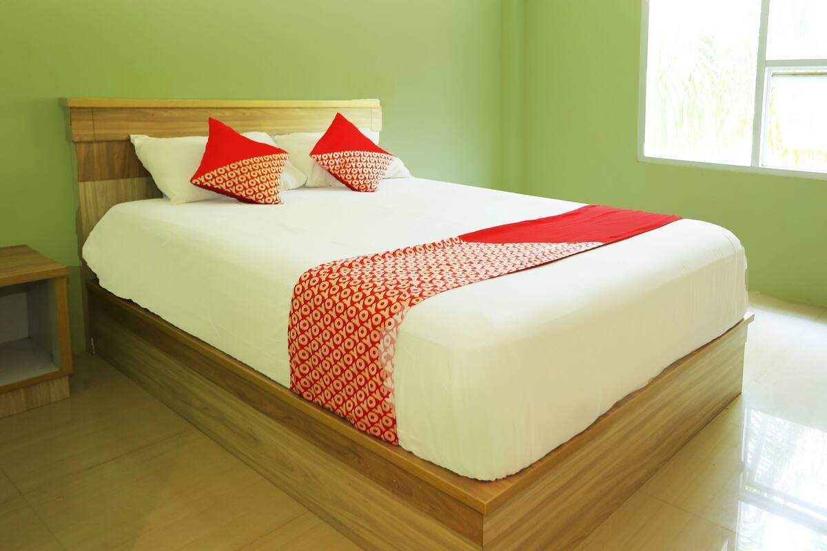 A neatly made bed with a wooden headboard, white bedding, and red and white patterned pillows.