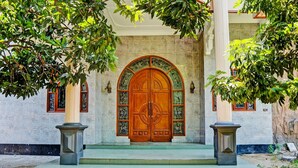 A grand entrance with a large wooden door, flanked by two columns and surrounded by lush greenery. - SPOT ON 93144 Homestay H. Syarif Syariah - Bandar Gresik 2 (Gresik)
