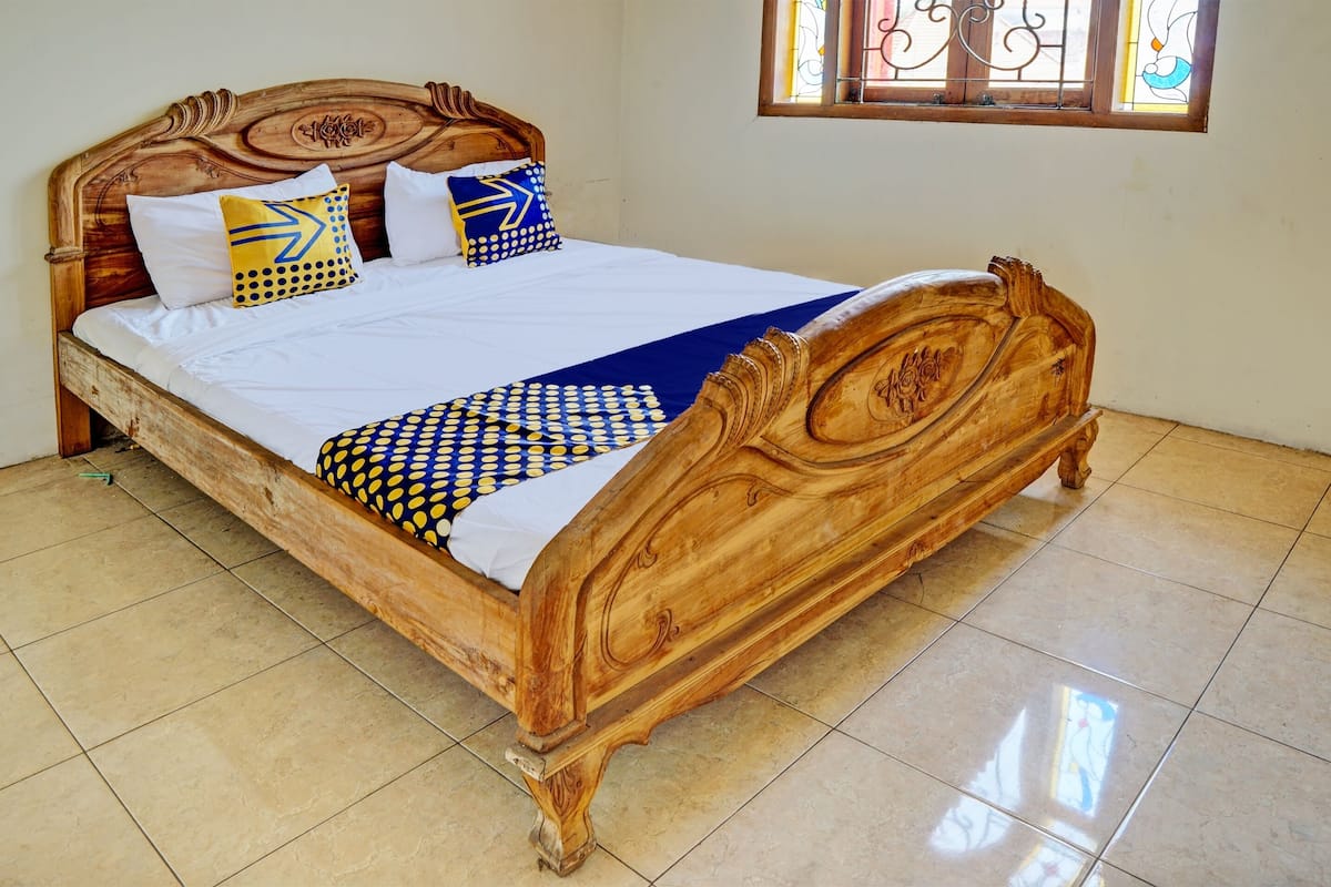 Un lit en bois avec une couvre-lit à motifs blancs et bleus, deux oreillers aux motifs bleus et jaunes, et une tête de lit en bois.