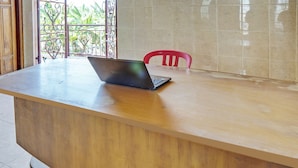 A wooden reception desk with a laptop, a red chair, and a view of greenery through a metal gate. - SPOT ON 93144 Homestay H. Syarif Syariah - Bandar Gresik 2 (Gresik)