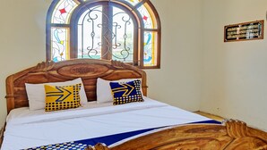A bedroom with a wooden bed, two pillows with geometric patterns, a stained glass window, and a wall plaque. - SPOT ON 93144 Homestay H. Syarif Syariah - Bandar Gresik 2 (Gresik)