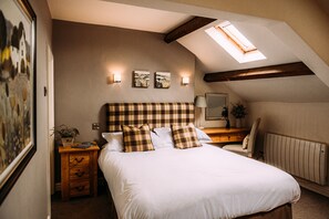 A bedroom with a large bed, a wooden nightstand, a desk, a chair, a radiator, and a skylight.