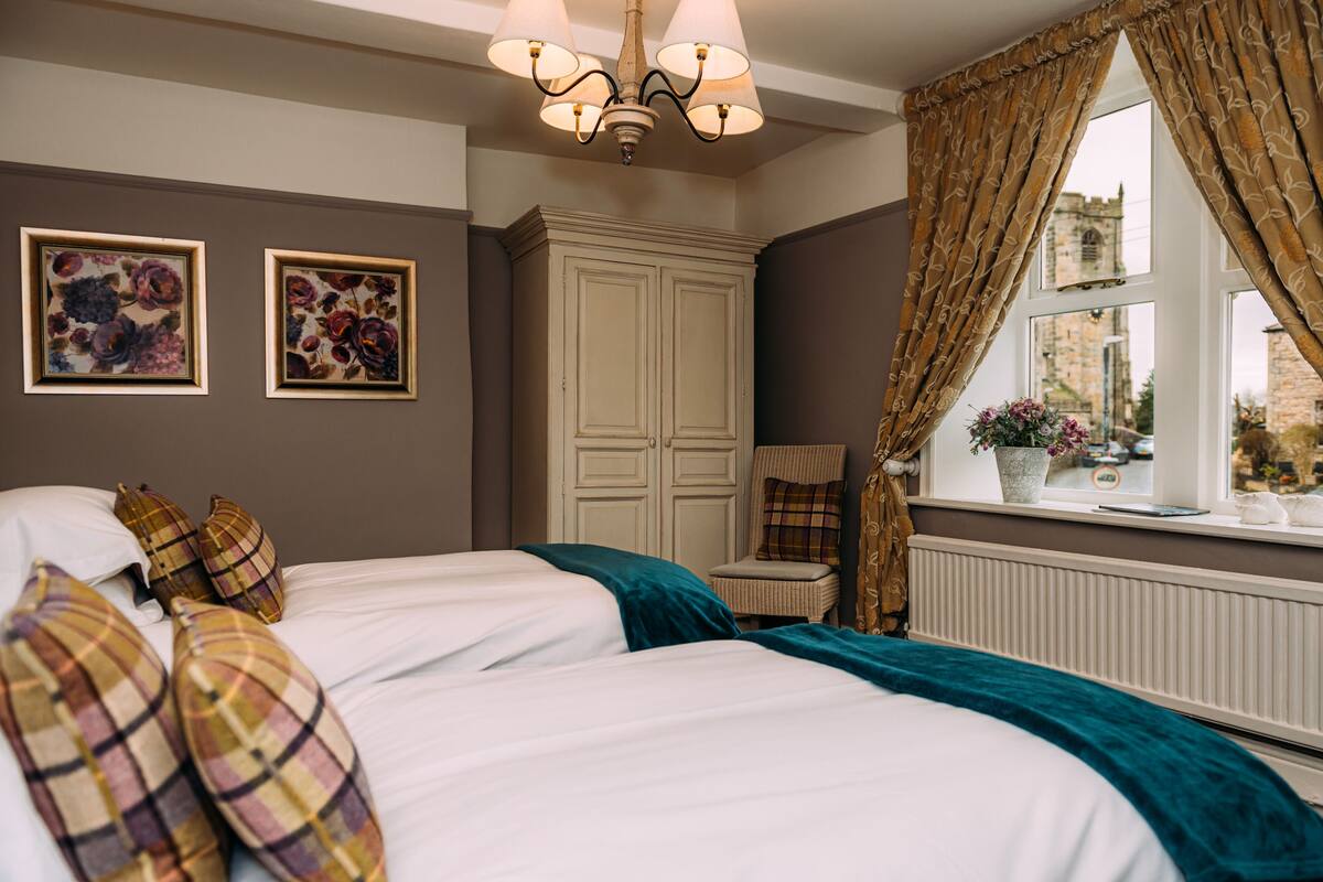 A bedroom with two beds, a wardrobe, a chair, and a window with curtains.