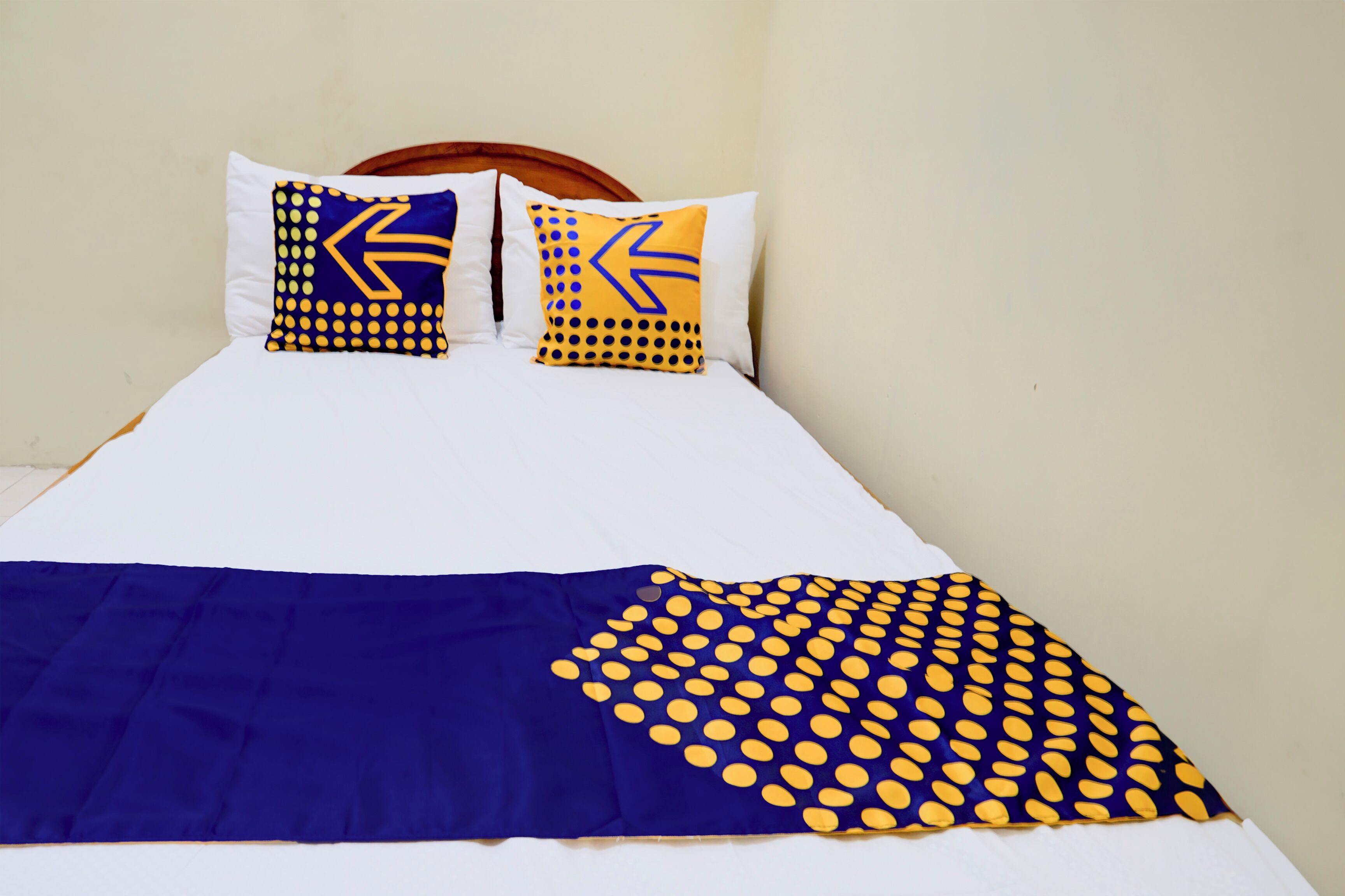 A bed with a blue and yellow polka dot blanket and two pillows with similar patterns.