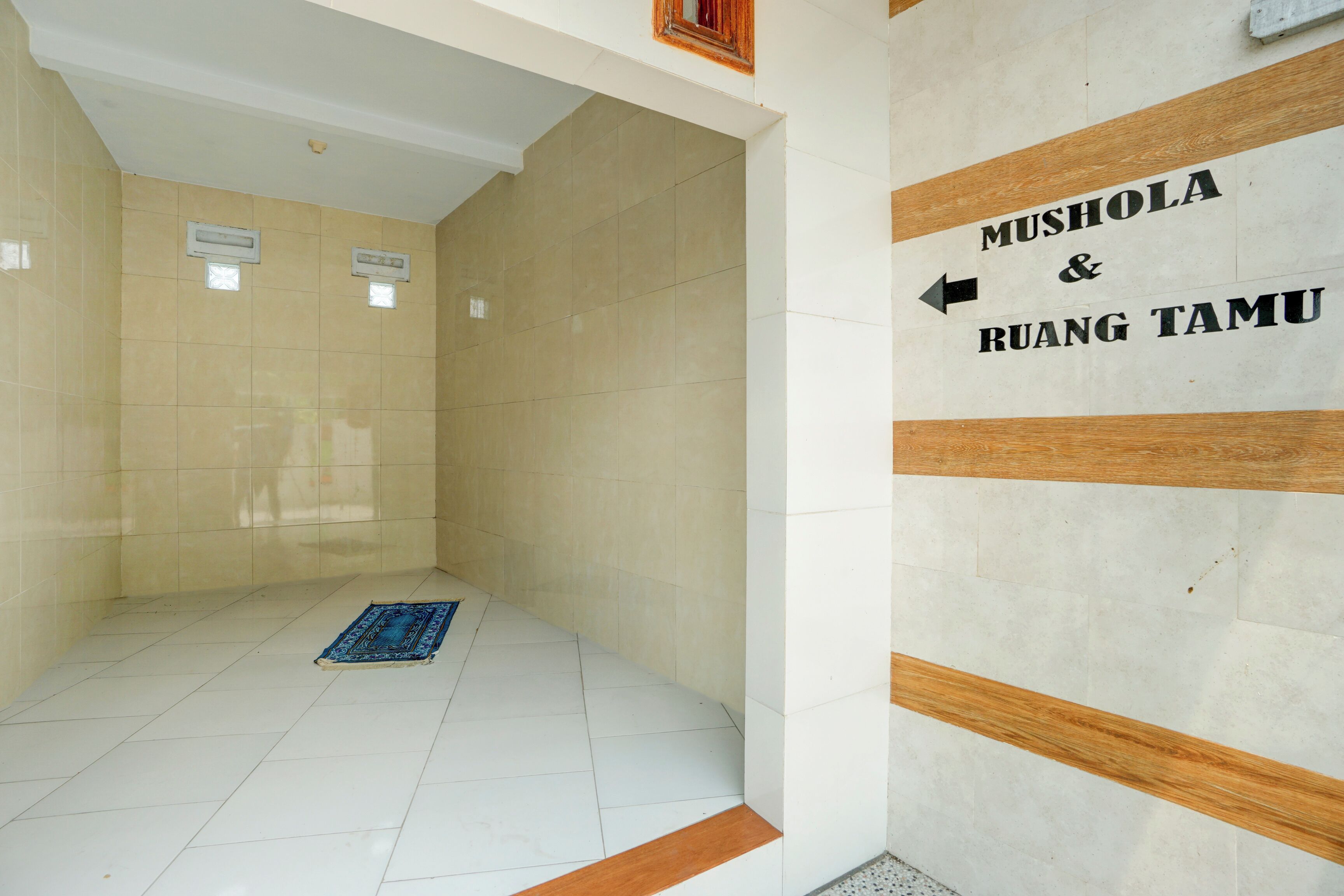 A hallway with a directional sign pointing to 'Mushola & Ruang Tamu'.