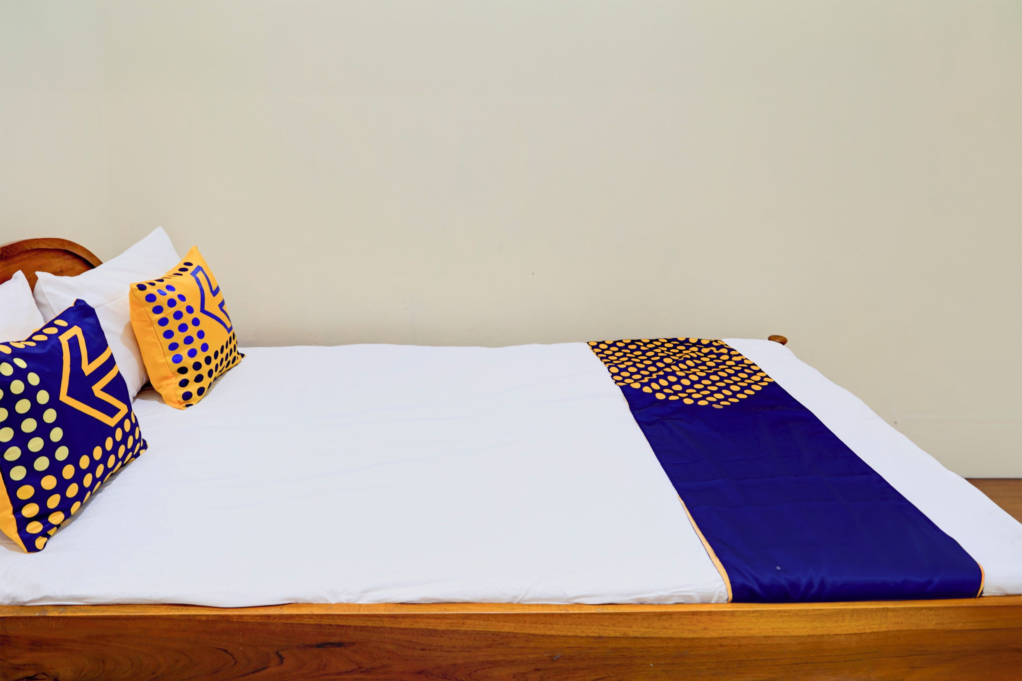 Cama bem arrumada com roupa de cama branca e azul, duas almofadas estampadas e uma cabeceira de madeira.