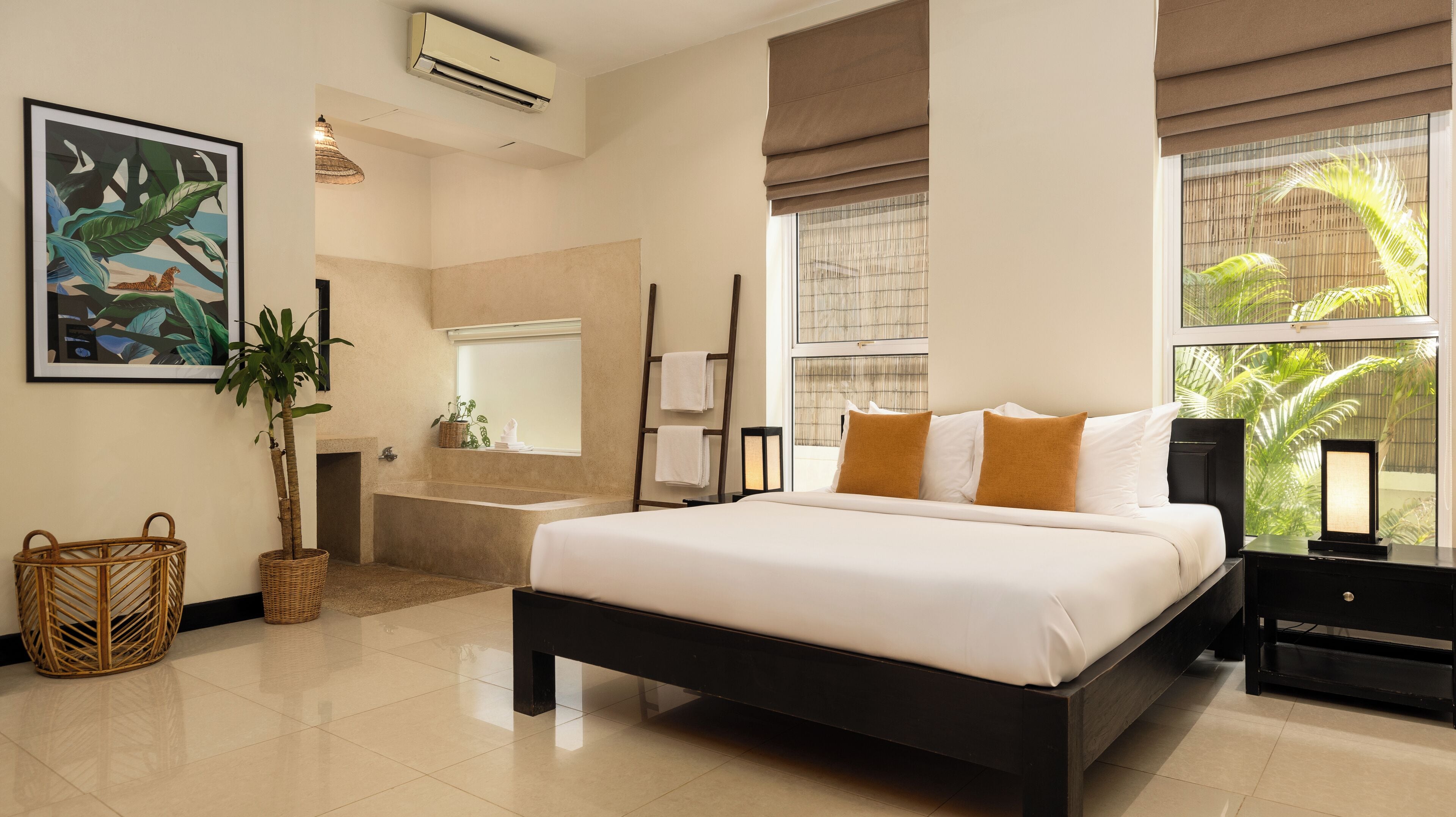 A modern hotel room with a large bed, a bathtub, a large window with a view of palm trees, a wall-mounted air conditioner, and a framed tropical painting.