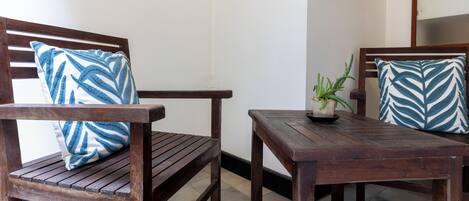 Un banco de madera con un cojín de diseño azul y blanco, una mesita con una planta en maceta, y otro banco con un cojín similar.