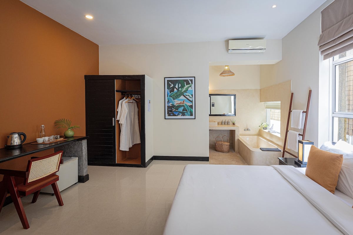 Hotelkamer met een bed, een bureau met stoel, een kledingkast, een badkamer met bad en een raam met gordijnen.