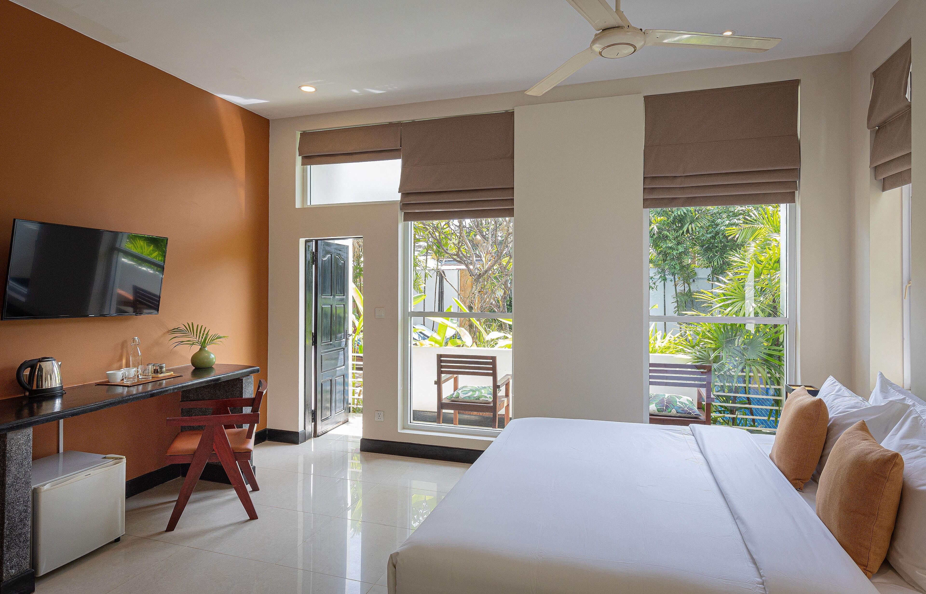 A bedroom with a bed, a desk with a chair, a TV, and a view of the outdoors.