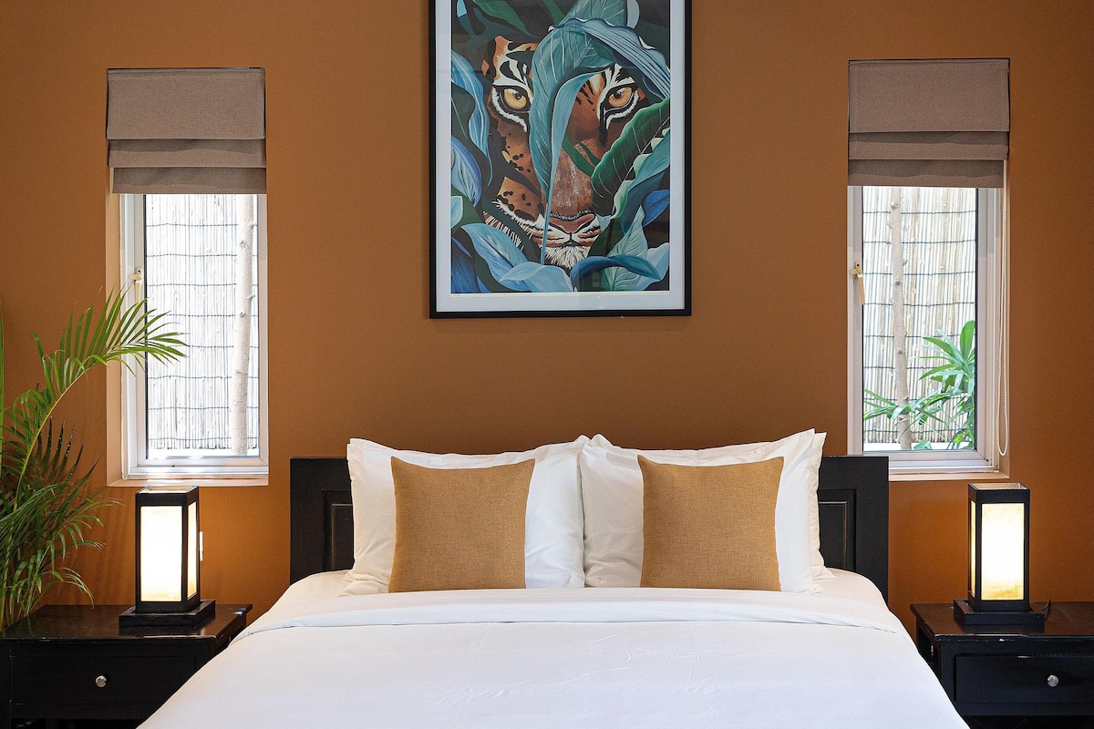 Een slaapkamer met een groot bed, een plafondventilator, een schilderij en twee bedlampjes.