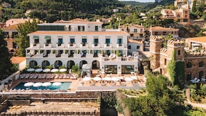 A hotel with a pool, outdoor seating, and a view of the surrounding hills. - Château de Théoule Hôtel & Spa (Theoule-sur-Mer)
