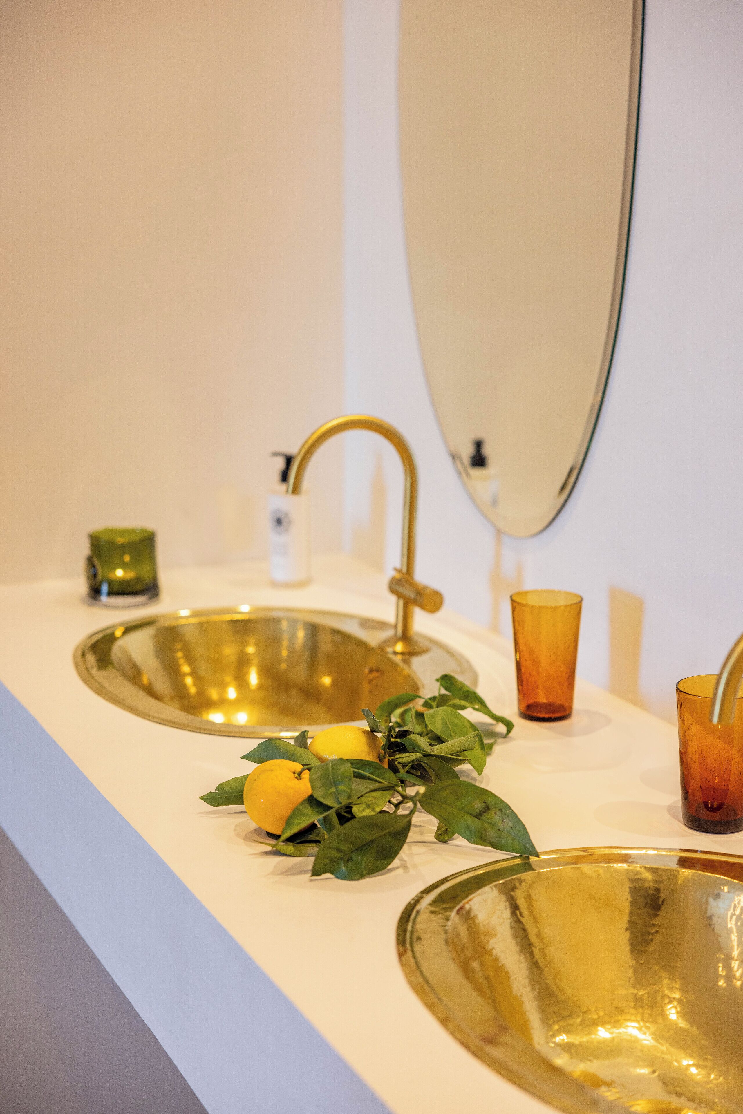 Een badkamer met twee gouden wasbakken, een spiegel en een kleine groene kaars op het aanrecht.