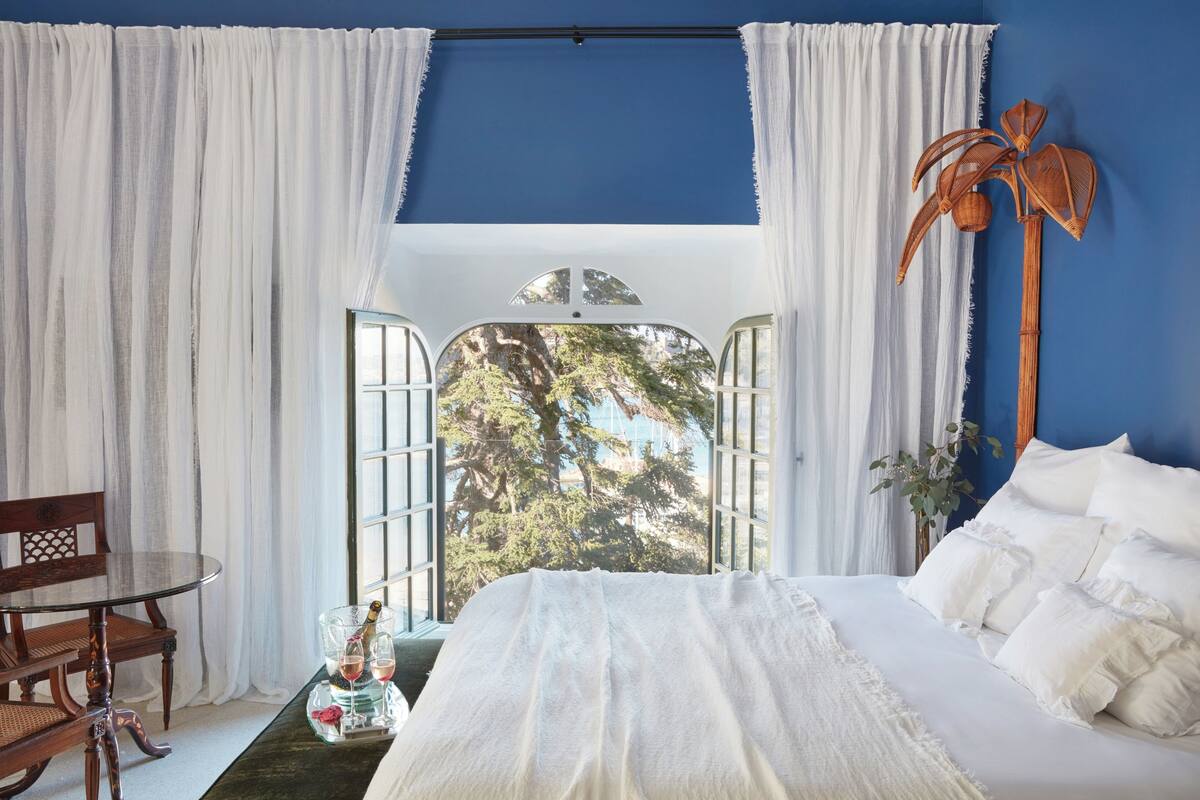 Ein Schlafzimmer mit einem Bett, einem Tisch mit Flasche und Gläsern sowie einem Sessel.