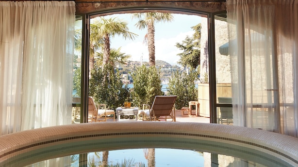 Un área de piscina con borde curvo, vista a palmeras y mobiliario exterior.