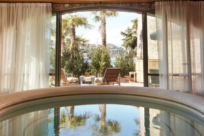 A pool area with a curved edge, a view of palm trees, and outdoor furniture. - Château de Théoule Hôtel & Spa (Theoule-sur-Mer)