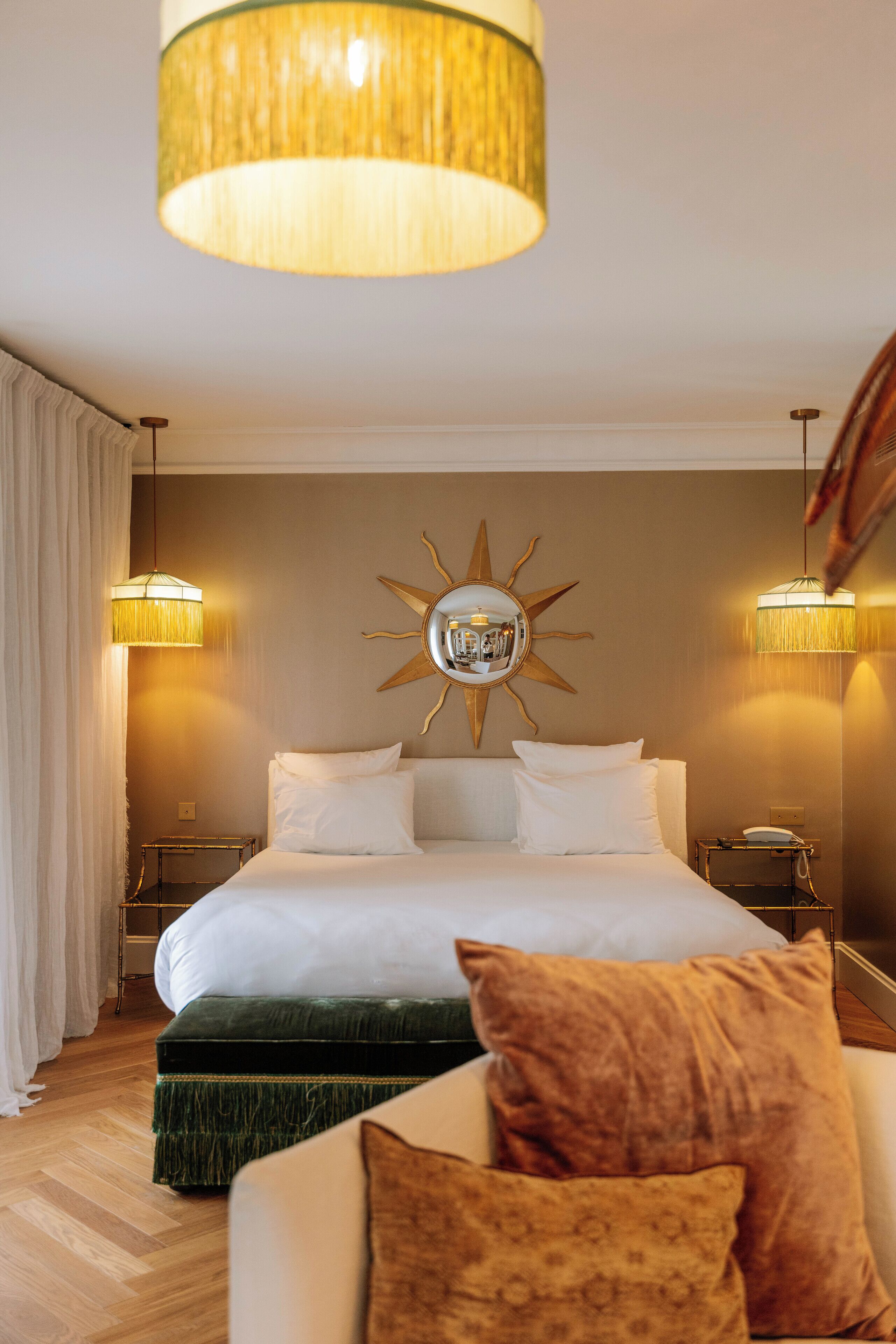 Een hotelkamer met een groot bed, twee bedlampen, een spiegel met zondecoratie en een houten vloer.