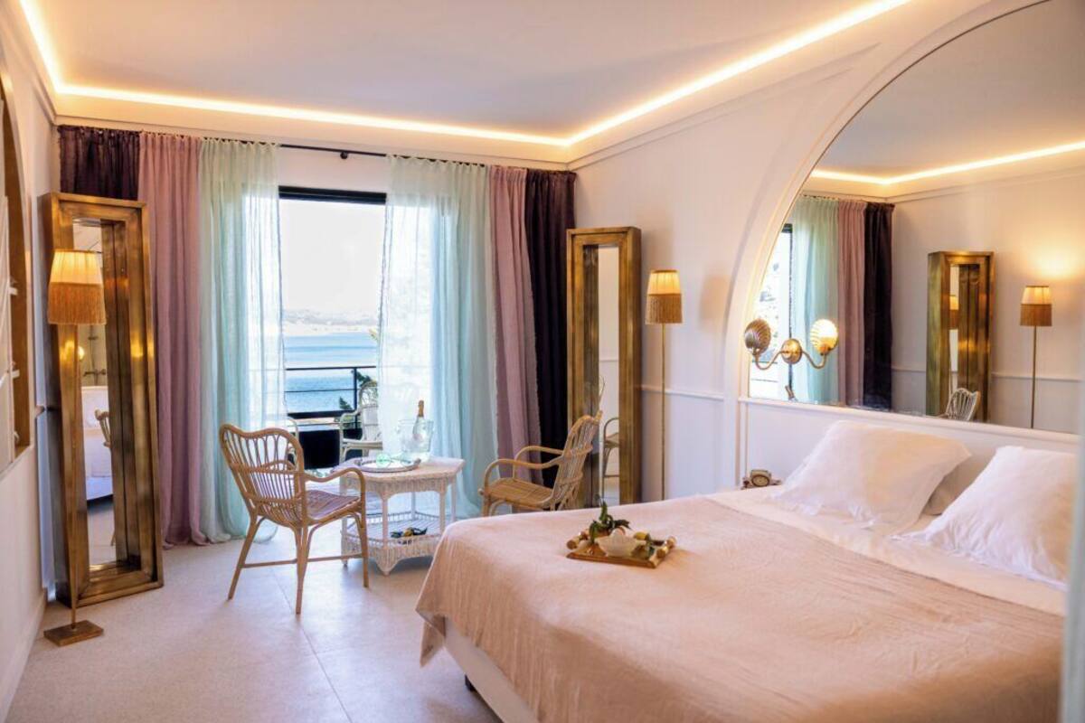 Ein Hotelzimmer mit einem großen Bett, einem kleinen Tisch, zwei Stühlen und Meerblick.