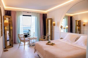 Habitación de hotel con una cama grande, una mesita, dos sillas y vista al mar.