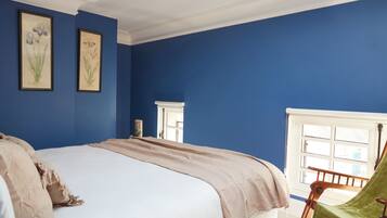 Un dormitorio con una cama grande, paredes azules, una ventana y dos cuadros florales enmarcados.