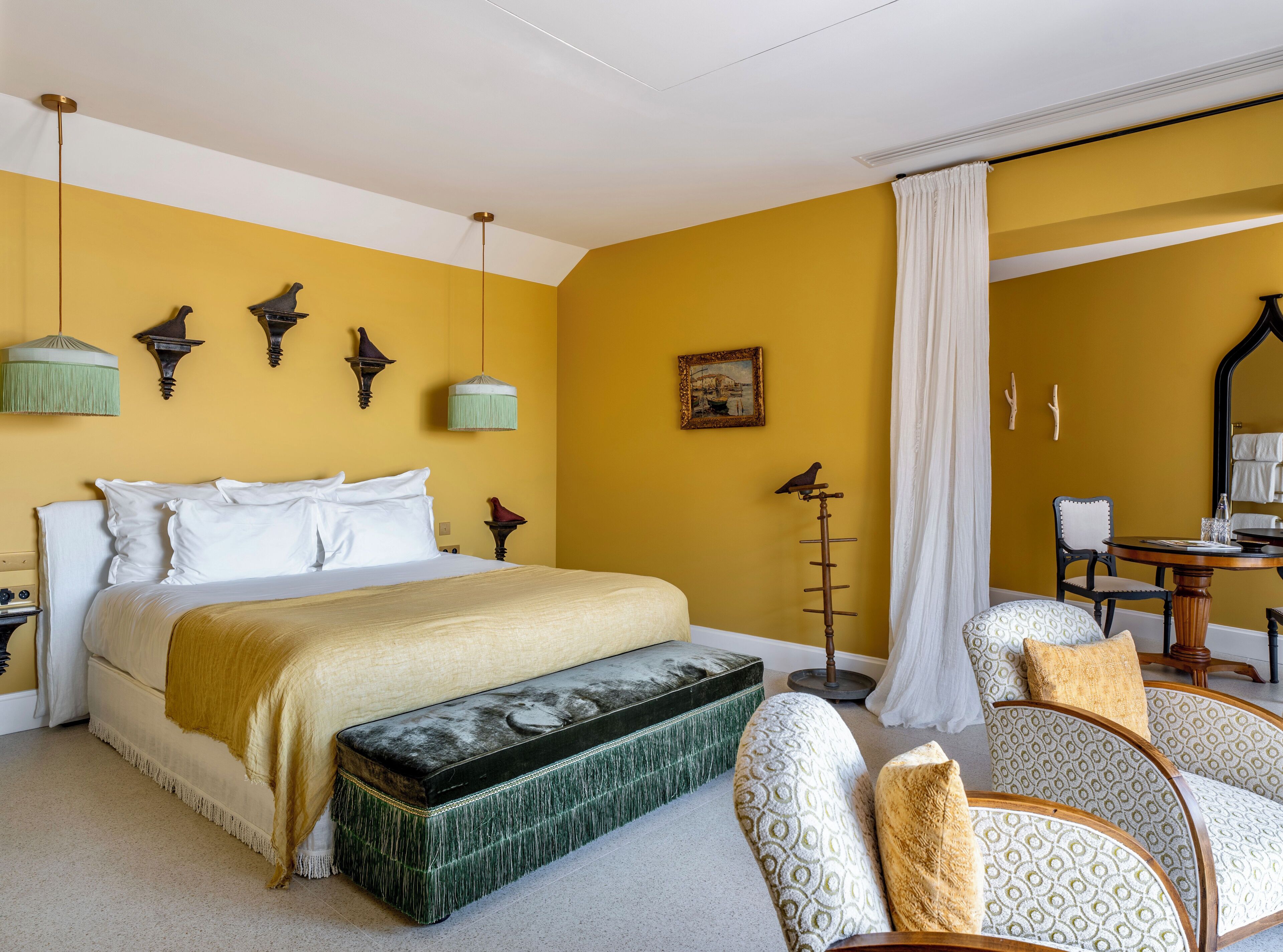 Ein Zimmer mit einem Bett, einer Bank, einem Stuhl, einem Tisch und einem Spiegel.