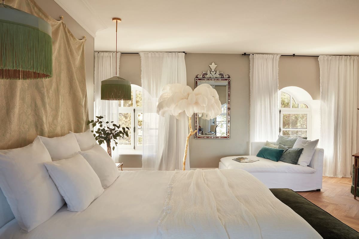 Ein Schlafzimmer mit einem großen Bett, einem Schlafsofa, einem Spiegel und einem Fenster mit Vorhängen.