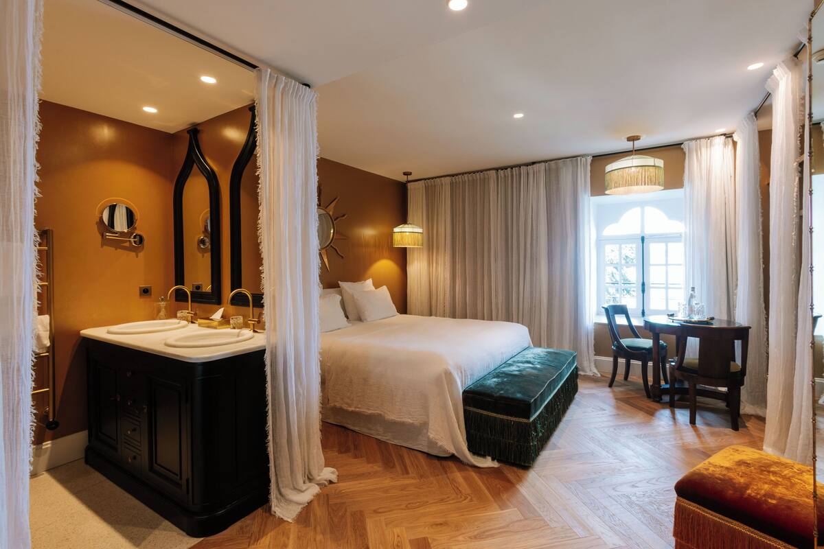 Ein Hotelzimmer mit einem großen Bett, einem Schminktisch mit Spiegel, einem Schreibtisch und einem Fenster mit Vorhängen.