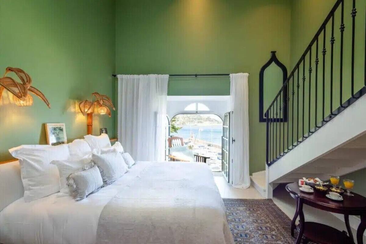 Ein Schlafzimmer mit einem Bett, einem Tisch mit Frühstücksgebäck, einer Treppe und Blick ins Freie.
