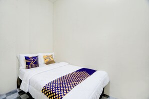 Een enkel bed met wit beddengoed en twee sierkussens met geometrische patronen.