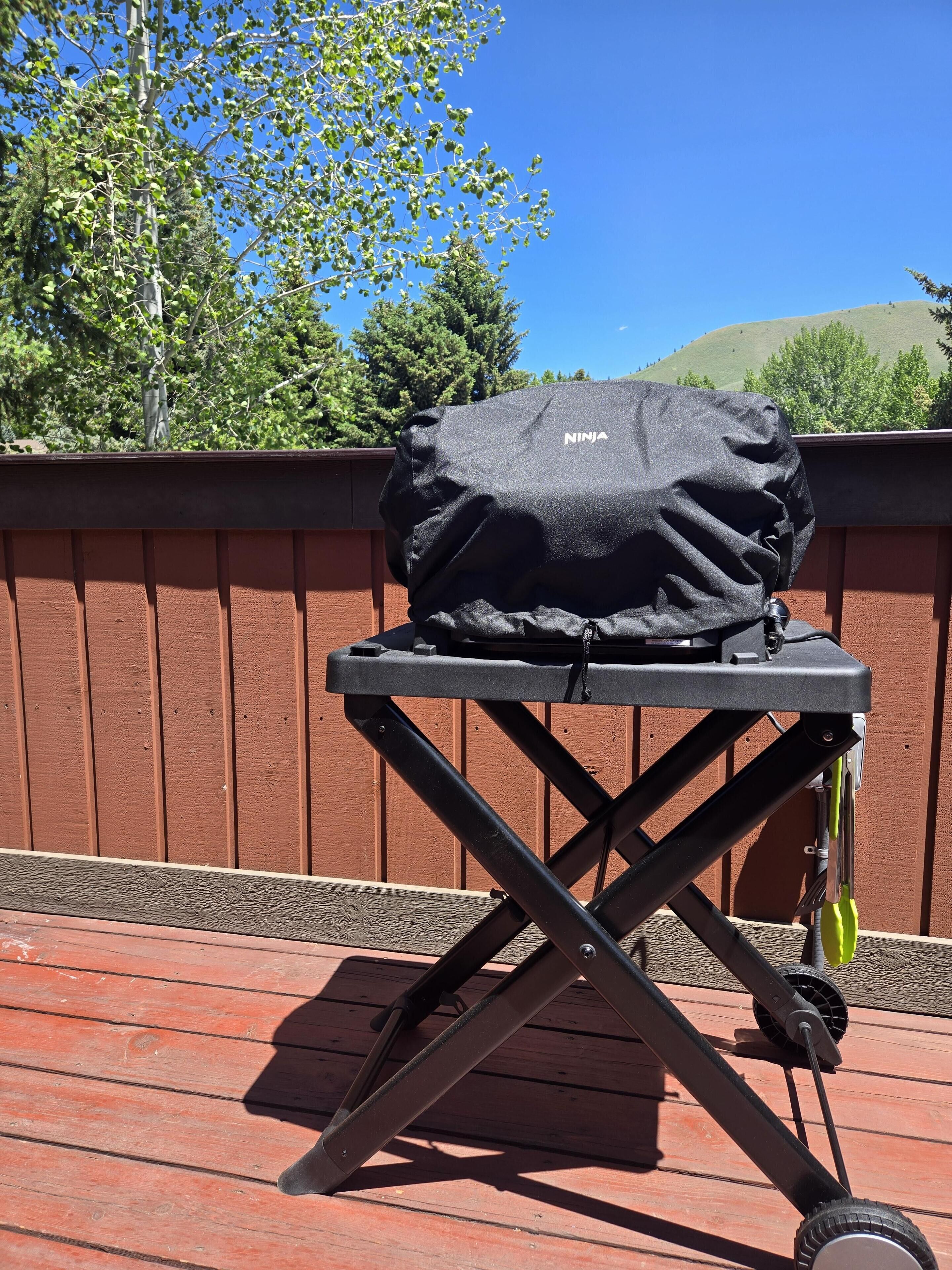 Un barbecue portable sur une terrasse en bois, avec une clôture marron et des arbres en arrière-plan.